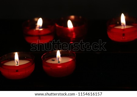 View of a red candles row in a church. Black dark background. Abstract picture with circular shapes and several flames. Colorful candlelight image. Contrasted colors.