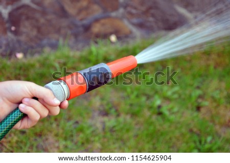 Concept of a hand holding a hose end and sprinkling the garden with water