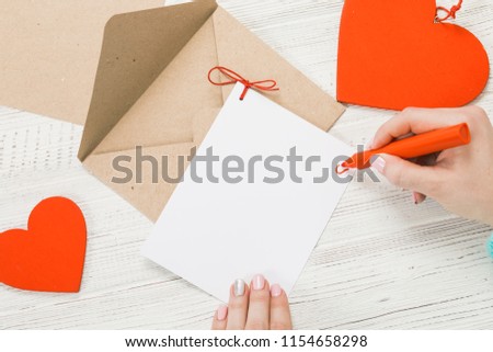 Hand of girl writing love letter on Saint Valentines Day. Handmade postcard with red heart shaped figure. 14 February holiday celebration. Valentine day concept with copy space.