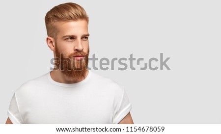 Serious thoughtful male with ginger beard, dressed casually, focused somewhere, isolated over white background with free space on right for your advertising content. Pensive red haired hipster Royalty-Free Stock Photo #1154678059