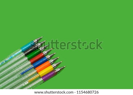 row of new bright colored pens lying on a green background. concept of office accessories. free space for advertising text
