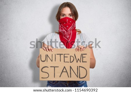 Womens right concept. Attractive serious young woman holds plate, wears casual clothes and red stylish bandana on face, belongs to feminist move, defenses females, isolated over white background