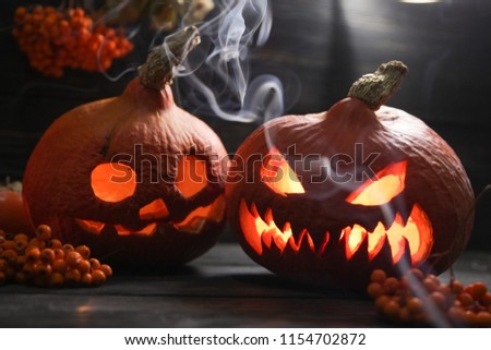 scary halloween pumpkin lanterns with luminous scary faces with rowanberries on a wooden background and the clouds of smoke in front of them