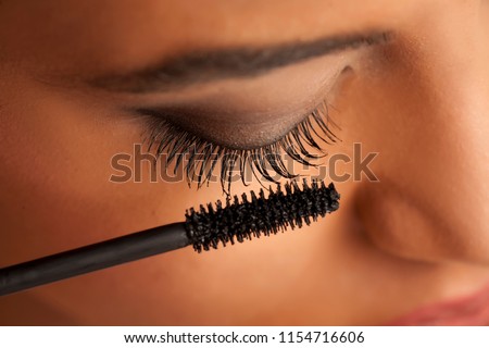 closeup of a young dark-skinned woman applying mascara on a white background Royalty-Free Stock Photo #1154716606