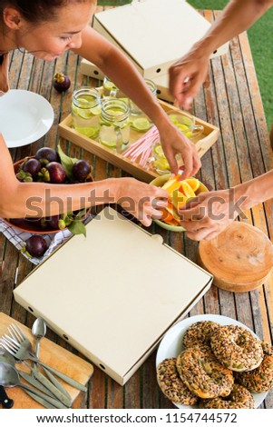 Two women prepare lunch on terras Pizza snack tropical fruits mangosteen orange healthy donuts summer cool drink with a lime on wooden table. Top view. Open air picnic