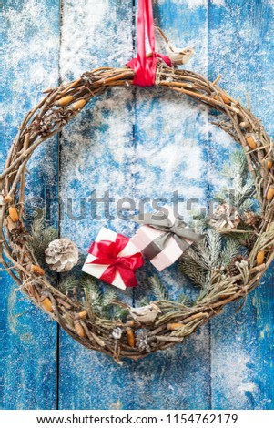 Christmas wreath with baubles, toy bird, cones and evergreen boughs on a blue wooden door. Decorations with furry spruce little gift box, red ribbon, acorns, cones, snow.