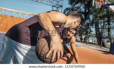 Two young men playing basketball at outdoor court.