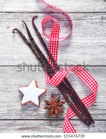 Country spices background with a colourful fresh red and white decorative ribbon twirled artistically through vanilla pods, star anise, and a Christmas star cookie on a weathered wood backgorund