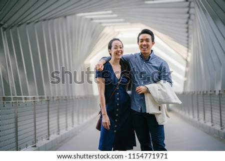 A portrait of a young and attractive Chinese Asian couple smiling and holding one another. They are in their thirties and are both well-dressed, well-groomed and confident about their future.