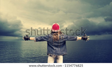 A teenage girl with widely spaced arms. Denim clothing. Baseball cap. Against the background of the sea and beautiful clouds. The concept of success. Background.