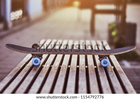 Close-up photo of a skateboard that standing on a bench on the embankment during beautiful sunset.