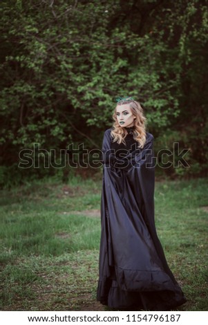 The concept of Halloween. A witch in black robes and green lips among the forest. Witchcraft and magic. Photo for your design.