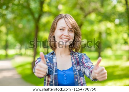 Portrait of young beautiful woman happily raises his thumb up and smiling, on green background summer nature