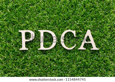 Wood alphabet in word PDCA (plan do check act) on artificial green grass background