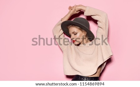 Portrait of woman posing wearing cosy sweater on pink background. Fashion photo shoot of naturally beautiful girl in trendy hat.