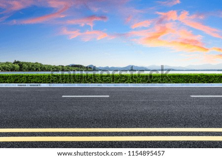Asphalt road and lake with mountains at beautiful sunset