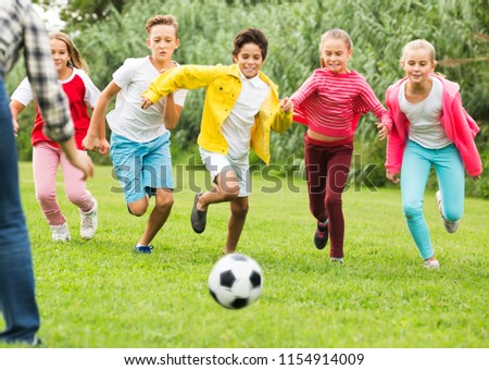 Company of glad children playing football on the playground in park