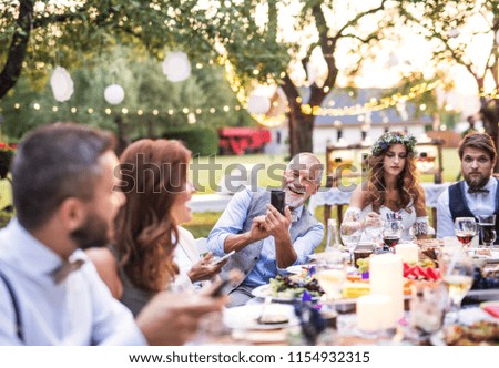 A senior man taking selfie at the wedding reception outside in the backyard.