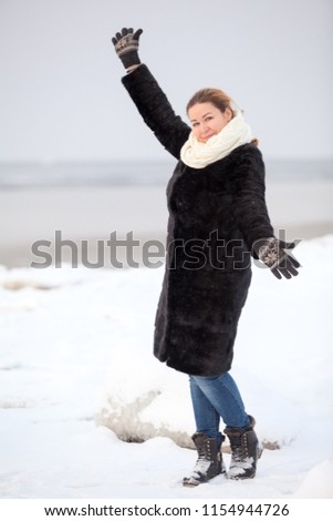 Happy young woman with raised hands. Wears fur coat, winter season