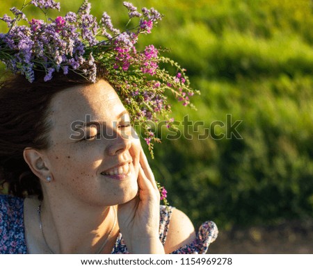 portrait of a young girl's face, in a field with a wreath of live wild flowers on her head, in the afternoon outdoors