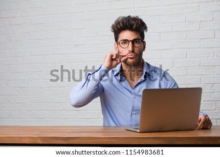 Young business man sitting and working on a laptop keeping a secret or asking for silence, serious face, obedience concept