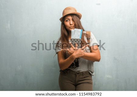 Portrait of young traveler latin woman against a wall confused and doubtful, decide between two options, concept of indecision. Holding her passport and boarding pass.
