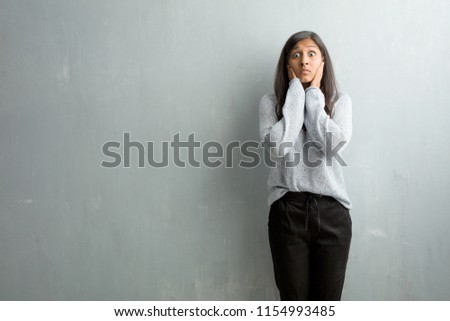 Young indian woman against a grunge wall covering ears with hands, angry and tired of hearing some sound