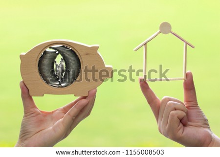 Woman hand holding stack of coins money in piggy bank wood and holding wooden house on natural green background,Saving money for new home and real estate investments concept