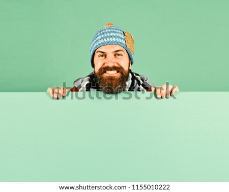 Autumn and cold weather concept. Hipster with beard and happy face wears warm clothes. October and November sale idea. Man in warm hat on green background, copy space.