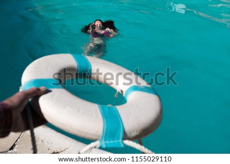 Man's holding out a life preserver out to save a Caucasian woman with dark hair from drowning in a swimming pool. Cry for help man tries to save a woman who can't swim. Girl drowning in pool.
