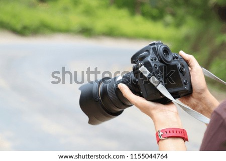 Closeup of a black digital single lens reflection camera carried by woman's hands with natural blackground in sunny day.