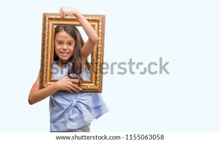 Brunette hispanic girl holding vintage art frame annoyed and frustrated shouting with anger, crazy and yelling with raised hand, anger concept