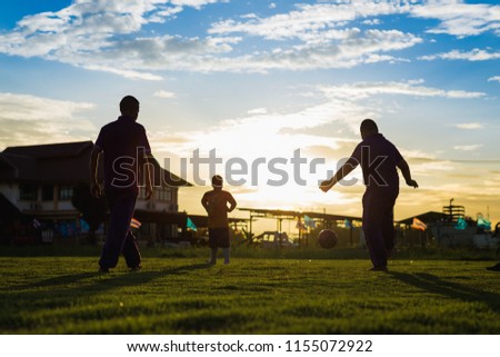 An action picture of a group of kids playing soccer football for exercise in community rural area under the sunset.