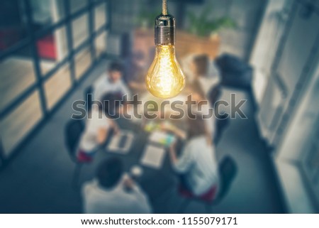 Young business people are discussing together a new startup project. A glowing light bulb as a new idea.