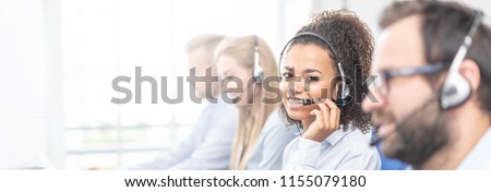 Call center worker accompanied by her team. Smiling customer support operator at work. Young employee working with a headset. Royalty-Free Stock Photo #1155079180