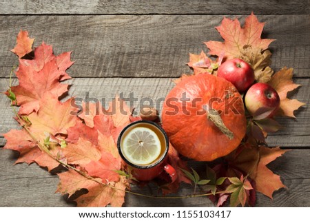 Warming cup of tea with decor of autumn leaves and pumpkins on wooden board. Fall still life.