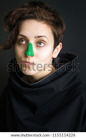 photo portrait of a girl with curly short hair and green paint on her nose in black clothes with high collar grimaces dark background