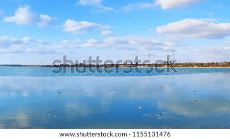 Beautiful colorful view of the Partwitzer lake beach in Germany, floaded sand quarry, blue azure water with mirror water surface, the bright blue sky with clouds is reflected in the watery surface
