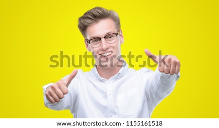 Young handsome blond man approving doing positive gesture with hand, thumbs up smiling and happy for success. Looking at the camera, winner gesture.