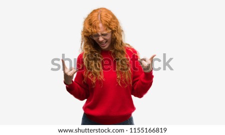 Young redhead woman wearing red sweater shouting with crazy expression doing rock symbol with hands up. Music star. Heavy concept.