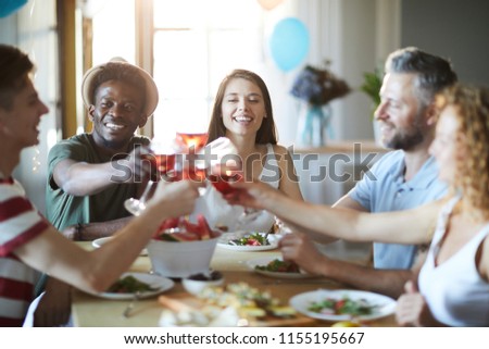 Happy intercultural friends gathered by table for holiday celebration at home