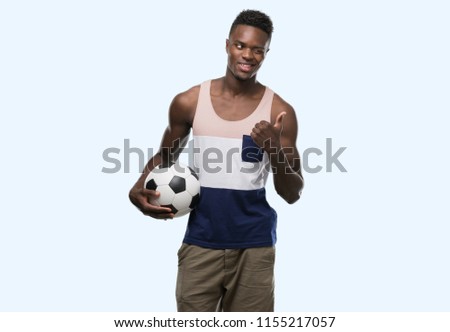Young african american man holding soccer football ball pointing with hand and finger up with happy face smiling