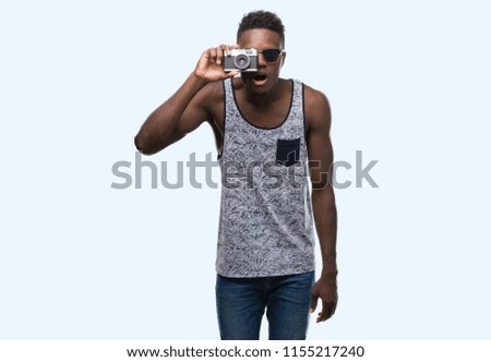 Young african american man holding vintage camera scared in shock with a surprise face, afraid and excited with fear expression