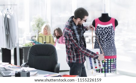 handsome fashion designer sitting with clothing sketches at the studio full of tailoring tools and clothes