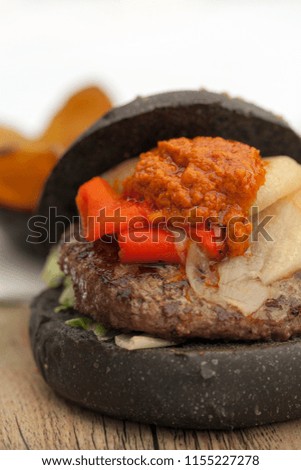
Hamburger with a black bread roll, with peppers, with lettuce and mayonnaise and ketchup, served on a wooden board, against a light background and selective focus.