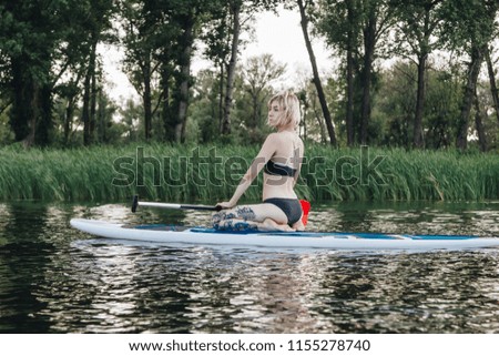 blonde tattooed girl sitting on paddle board on river