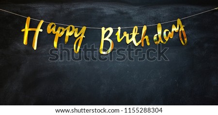 Happy birthday garland at a dark wall. The letters are golden
