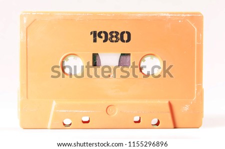 A vintage cassette tape from the 1980s era (obsolete music technology) with the text 1980 printed over it (my addition, not in the original image). Color: cream, sand. White background.

