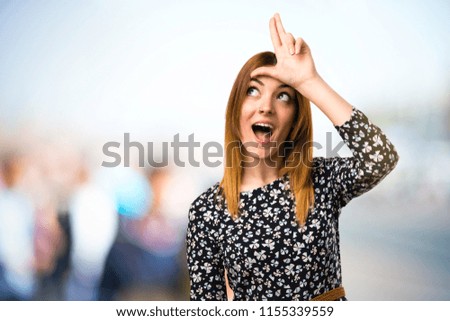 Beautiful young girl making loser sign on unfocused background
