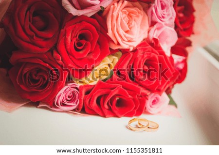 A pair of gold wedding rings lies next to the bouquet of the bride. Soft focus, toned picture.